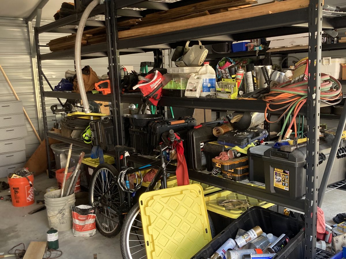 A garage with cluttered shelves and items stacked on the floor